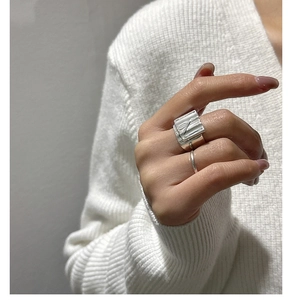 Detail of silver wavy textured rings worn on fingers against a white knit sweater background