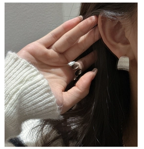 Detail of silver brushed matte curved earrings and oval gemstone rings worn with white knit