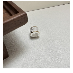 Detailed view of silver charm with gold edges and intricate floral engraving