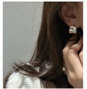 Close-up of a silver-toned wide C-shaped ear cuff with a polished mirror finish on model