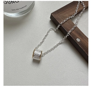 Detail of silver cylinder pendant with gold trim and embossed scroll pattern on O-chain