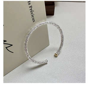 Detail of S925 silver open bangle with embossed vine patterns and golden sphere accent