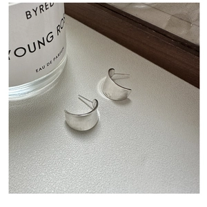 Macro detail of silver C-shaped textured earrings on a white surface with props