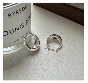 Macro shot of minimalist polished silver wide hoop earrings on a textured surface