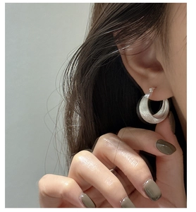 Macro view of wide C-shaped S925 silver earrings with a brushed matte texture on model