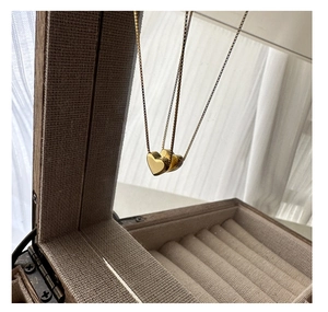 Gros plan d'un collier à pendentif cœur doré suspendu devant un miroir de coffret