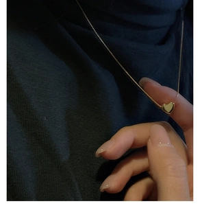 Détail d'un collier avec pendentif cœur doré minimaliste tenu entre les doigts poli miroir