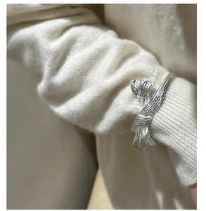 Close-up of a silver twisted butterfly ring with elegant silk texture on a white knit sleeve