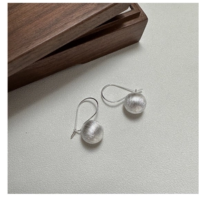 Macro detail of S925 sterling silver ball earrings featuring a brushed metal texture finish
