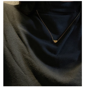 Collier avec pendentif coeur doré minimaliste sur un haut à col roulé noir tricoté