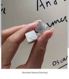Détail macro de boucles d'oreilles cubes en argent brossé au fini géométrique unique