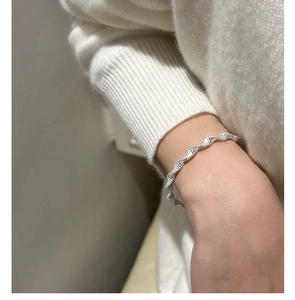 Close-up of a silver twisted wave texture bracelet on a wrist with a white sweater