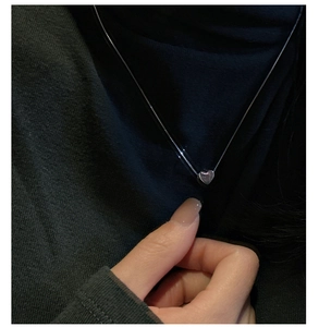 Détail d'un pendentif cœur en argent minimaliste porté sur une fine chaîne box