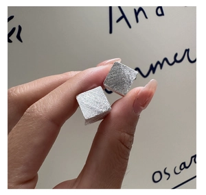 Détail de boucles d'oreilles carrées géométriques en argent S925 brossé avec texture mate