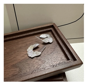 Detailed view of S925 sterling silver fan-shaped earrings with pleated texture on wood