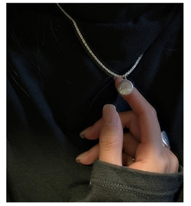 Detail of silver S925 necklace featuring a textured hammered round pendant on dark fabric