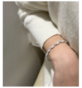 Macro shot of a twisted wave S925 sterling silver bangle on a soft knit sweater sleeve