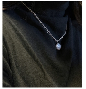 Close-up of baroque pearl pendant on shimmering silver chain worn over a dark sweater