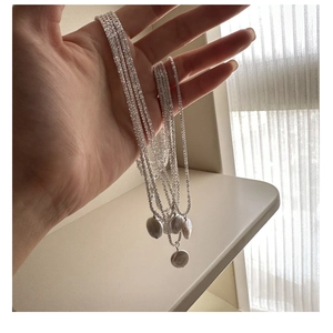 Macro detail of multilayer silver chain with baroque pearl pendants and weaving texture