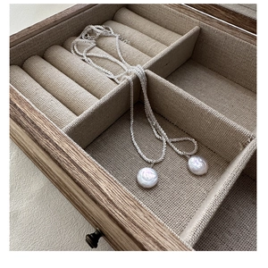 Detail of silver chain necklace with two baroque pearls on linen inside a wooden box
