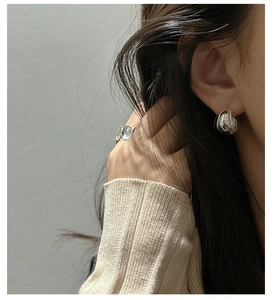 Detailed shot of silver curved earrings with beaded edges worn by a model in soft lighting