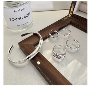 Artistic display of wavy silver earrings and ring in a wooden glass display case