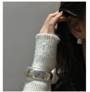 Detail of silver S925 curved wide metal stud earrings on a model in white sweater