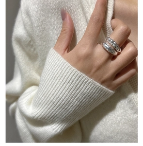 Macro detail of a silver croissant-style twist ring showing layered texture on a knit sleeve