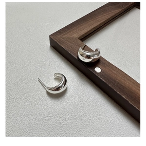 Detail view of silver C-shaped stud earrings with smooth finish and beaded inner edge