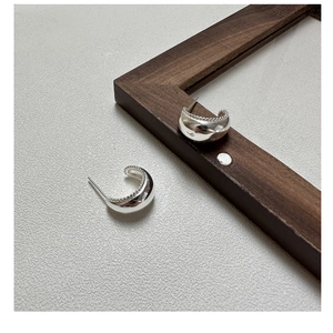 Detailed macro of C-shaped S925 silver stud earrings with fine milgrain edges on wood