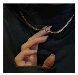 Macro shot of gold flat snake bone necklace with textured geometric pattern on a black sweater