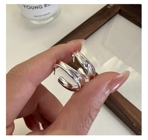 Macro detail of irregular curved silver hoop earrings held by hand for texture