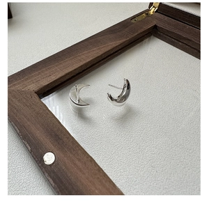 Vue macro de boucles d'oreilles lune minimalistes en argent S925 sur support bois