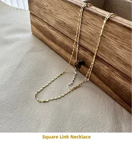 Close-up of minimalist gold and silver square link necklaces on a rustic wooden background