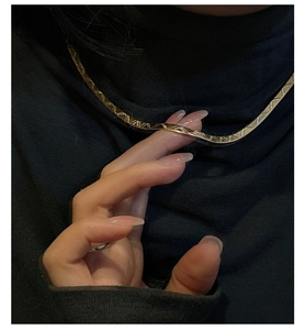 Detail of a gold flat snake chain necklace with chevron embossing on a black sweater