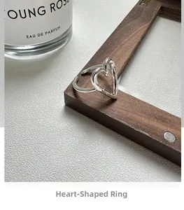 Close-up of a minimalist silver hollow heart ring leaning on a wooden frame