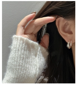 Close-up of stylish S925 silver thick curved hoop earrings worn by a model in soft light