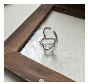 Macro detail of silver heart-shaped hollow ring on textured background with wooden frame