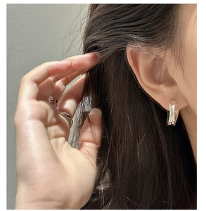 Close-up of minimalist silver curved earrings and sleek open rings on a female model
