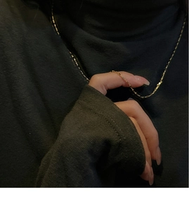 Close-up of a gold geometric square link necklace worn over a dark turtleneck sweater