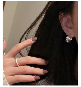 Détail de boucle d'oreille texturée en argent et bague en perles blanches sur mannequin