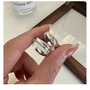 Detailed view of silver S925 fluid irregular curved hoop earrings held by hand