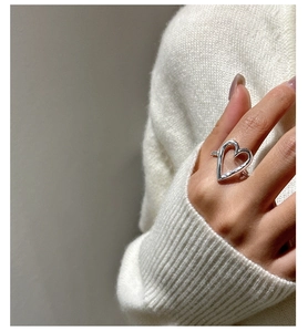 Close-up of minimalist hollow heart silver ring on finger with soft knit sweater