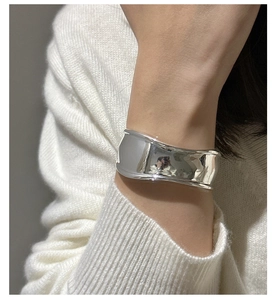 Close-up of wide polished silver cuff bracelet worn over a white knitted sweater sleeve