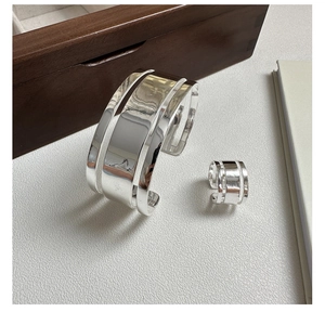 Macro shot of minimalist silver three-layer open ring and cuff bracelet on a wooden box