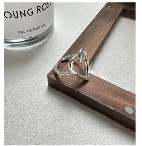 Macro shot of silver hollow heart ring on dark wood frame with perfume bottle decor