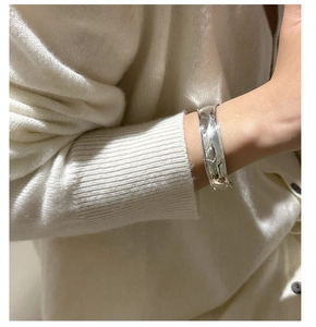 Close-up of a wide polished silver cuff bracelet worn over a creamy white knit sweater