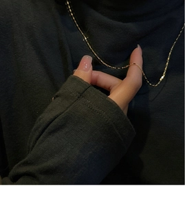 Close-up of gold geometric square link chain necklace worn on a black turtleneck