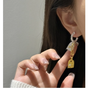 Close-up of S925 silver twist hoop earrings with gold chain and embossed charm details