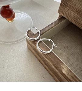 Close-up of polished S925 sterling silver hoop earrings on a wooden jewelry box